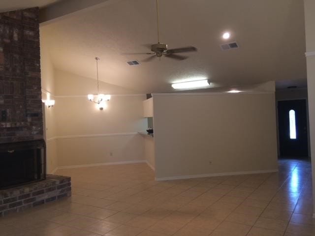 unfurnished living room featuring tile patterned flooring, vaulted ceiling, a brick fireplace, and ceiling fan with notable chandelier