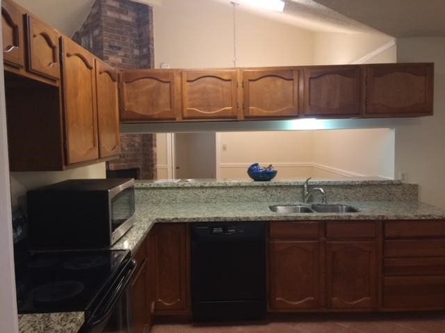 kitchen featuring sink, black dishwasher, lofted ceiling, and brick wall