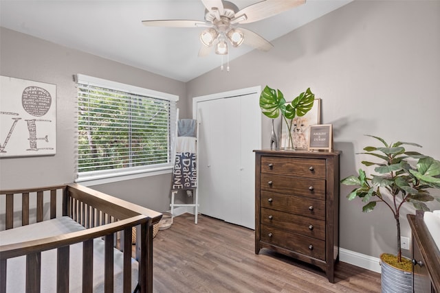 bedroom featuring a nursery area, lofted ceiling, a closet, ceiling fan, and hardwood / wood-style flooring