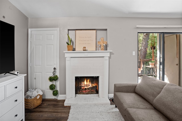 living room featuring dark wood-type flooring and a brick fireplace