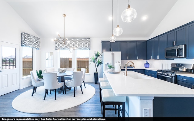 kitchen with appliances with stainless steel finishes, decorative light fixtures, dark hardwood / wood-style floors, sink, and a kitchen island with sink