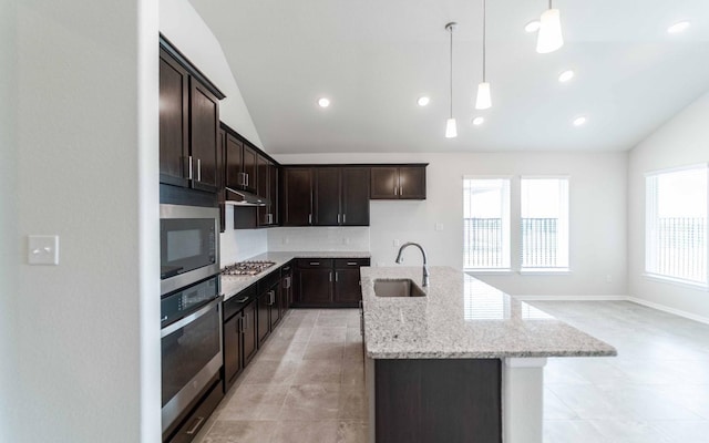 kitchen with sink, hanging light fixtures, a center island with sink, stainless steel appliances, and light stone countertops