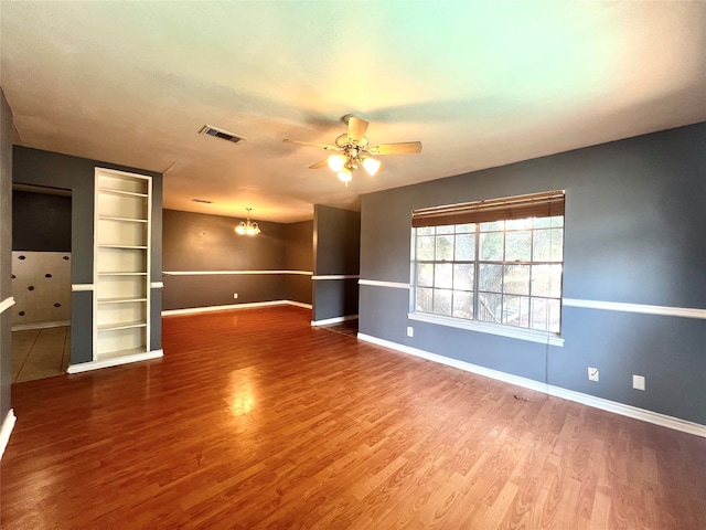 spare room featuring baseboards, visible vents, wood finished floors, and ceiling fan with notable chandelier