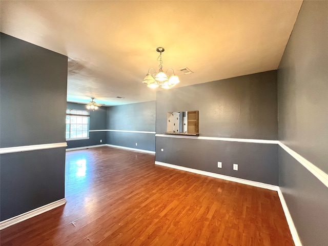 unfurnished room with ceiling fan with notable chandelier, visible vents, baseboards, and wood finished floors