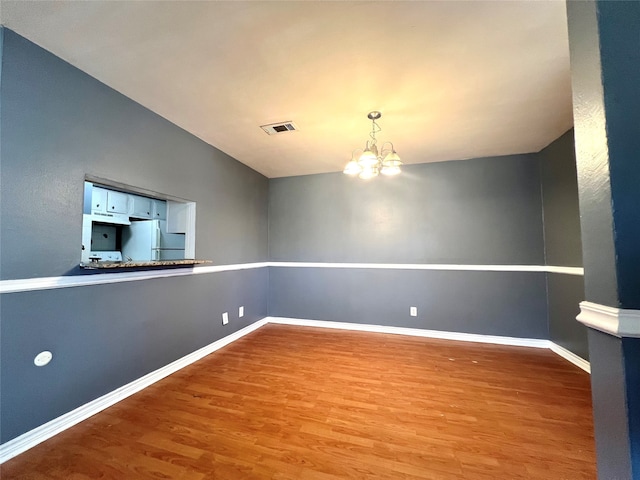 unfurnished room featuring a chandelier, wood finished floors, visible vents, and baseboards