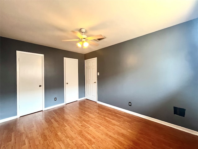 unfurnished bedroom with multiple closets, wood finished floors, a ceiling fan, and baseboards