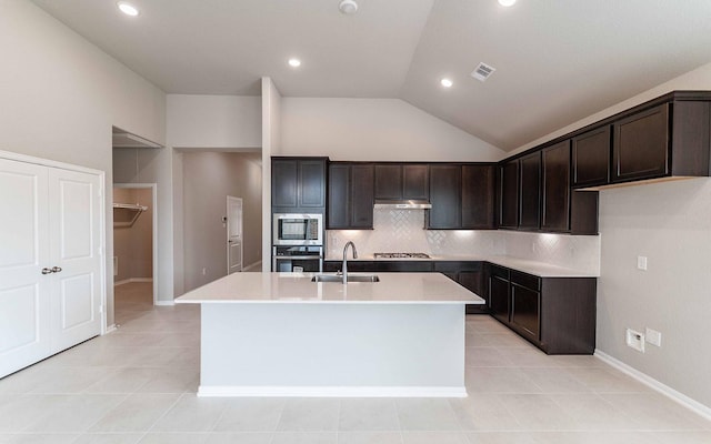 kitchen with dark brown cabinetry, sink, tasteful backsplash, stainless steel appliances, and a kitchen island with sink