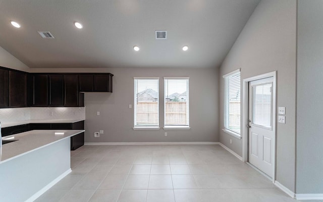 kitchen with lofted ceiling, light tile patterned floors, tasteful backsplash, and dark brown cabinetry