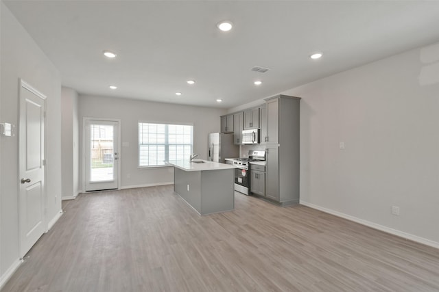 kitchen featuring sink, stainless steel appliances, an island with sink, gray cabinets, and light wood-type flooring