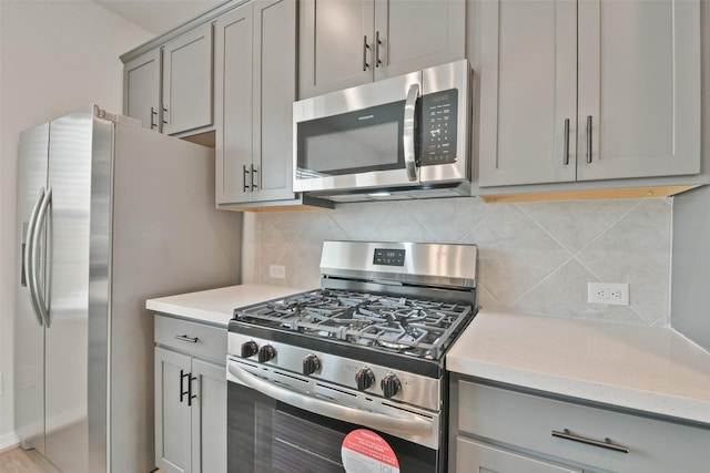 kitchen with decorative backsplash, appliances with stainless steel finishes, gray cabinets, and light stone counters