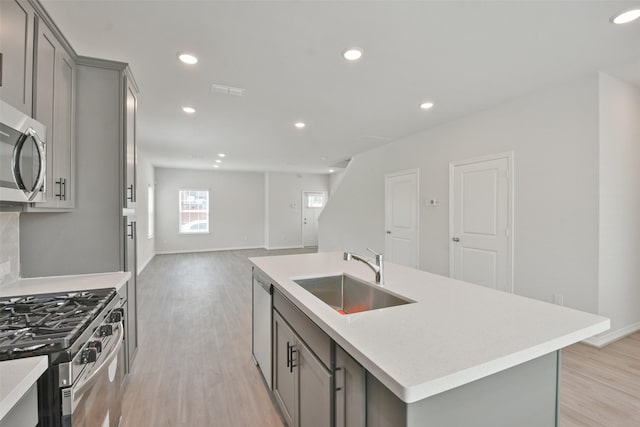 kitchen featuring sink, gray cabinets, a center island with sink, appliances with stainless steel finishes, and light wood-type flooring