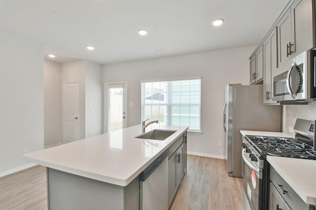 kitchen featuring appliances with stainless steel finishes, sink, light hardwood / wood-style flooring, gray cabinets, and an island with sink