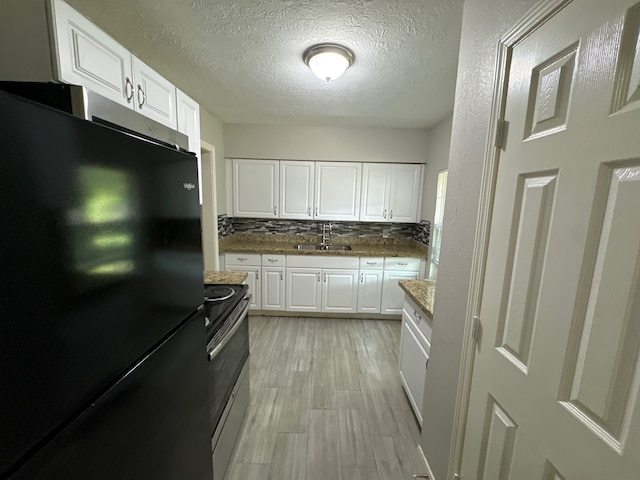 kitchen featuring black fridge, tasteful backsplash, stainless steel electric range oven, white cabinetry, and sink