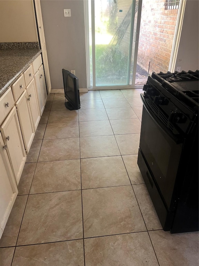 kitchen with light tile patterned flooring, light stone counters, white cabinetry, and black gas range oven