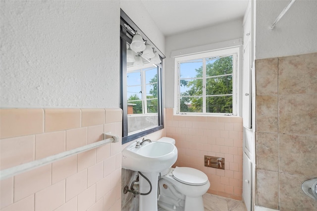 bathroom featuring toilet, a healthy amount of sunlight, tile patterned flooring, and tile walls