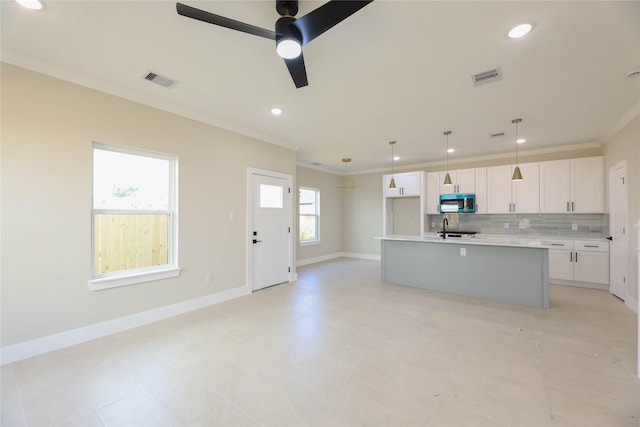 kitchen with decorative light fixtures, light countertops, stainless steel microwave, white cabinets, and an island with sink