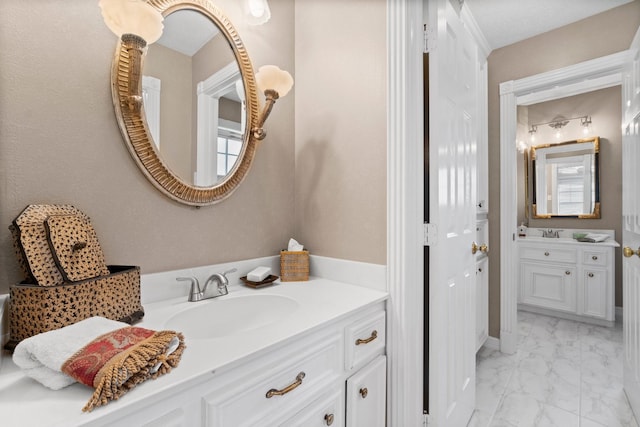 bathroom featuring marble finish floor, two vanities, and a sink