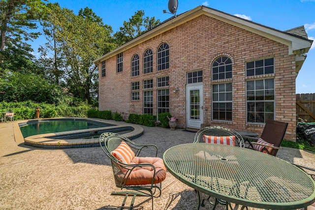 back of property with an outdoor pool, an in ground hot tub, fence, a patio area, and brick siding