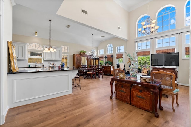 living area with light wood-type flooring, a towering ceiling, visible vents, and an inviting chandelier