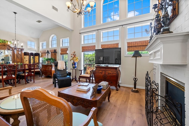 living area featuring light wood finished floors, visible vents, baseboards, a fireplace, and a notable chandelier