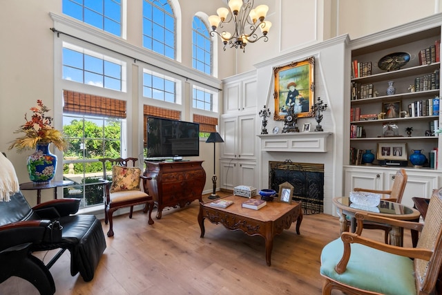 interior space with a chandelier, a high ceiling, a fireplace, built in features, and light wood finished floors