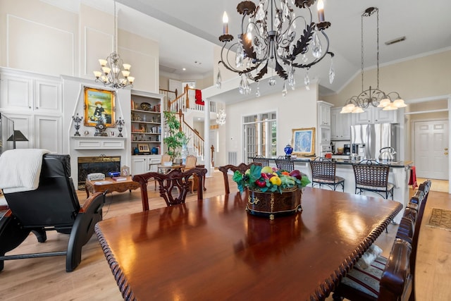 dining room featuring light wood finished floors, crown molding, a fireplace, and a notable chandelier