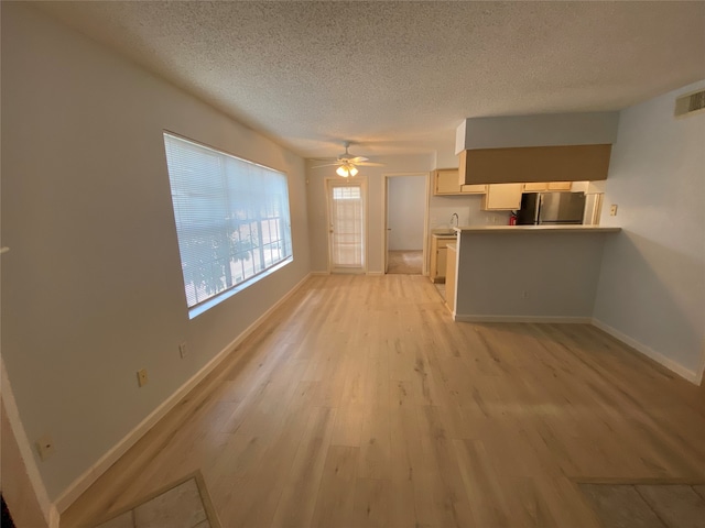 unfurnished living room with ceiling fan, sink, light hardwood / wood-style flooring, and a textured ceiling