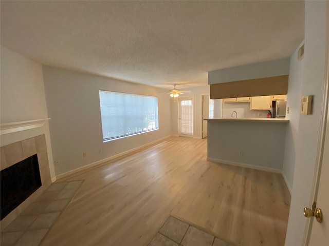 unfurnished living room featuring light wood-type flooring, a tile fireplace, a textured ceiling, and ceiling fan