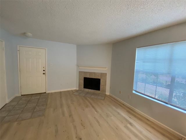 unfurnished living room featuring a textured ceiling, light hardwood / wood-style flooring, and a tiled fireplace