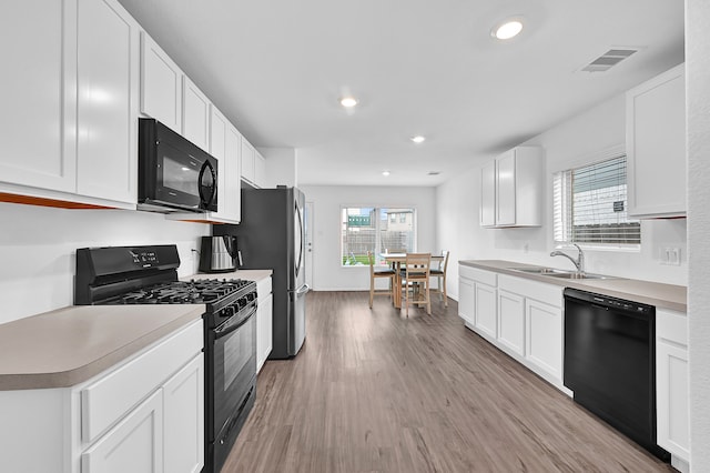 kitchen with light hardwood / wood-style floors, white cabinets, sink, and black appliances