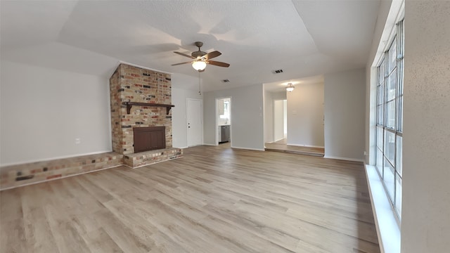 unfurnished living room featuring a fireplace, brick wall, ceiling fan, and light wood-type flooring