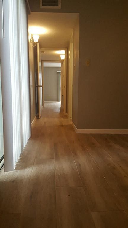 corridor with light wood-type flooring, visible vents, and baseboards