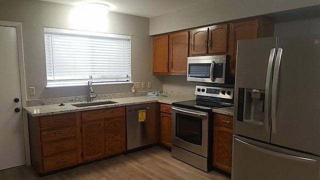 kitchen featuring brown cabinets, light wood finished floors, stainless steel appliances, a sink, and light stone countertops