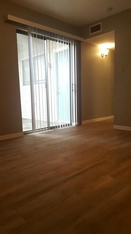 unfurnished room with baseboards, wood finished floors, and visible vents