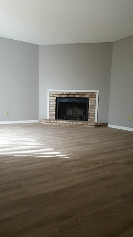 unfurnished living room with wood finished floors, a fireplace with raised hearth, and baseboards