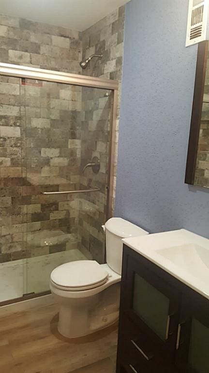 full bath featuring wood finished floors, a stall shower, vanity, toilet, and visible vents
