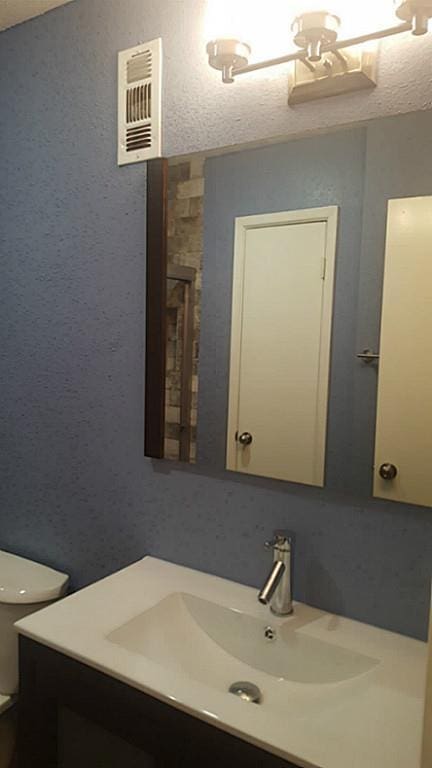 half bath with toilet, vanity, and visible vents