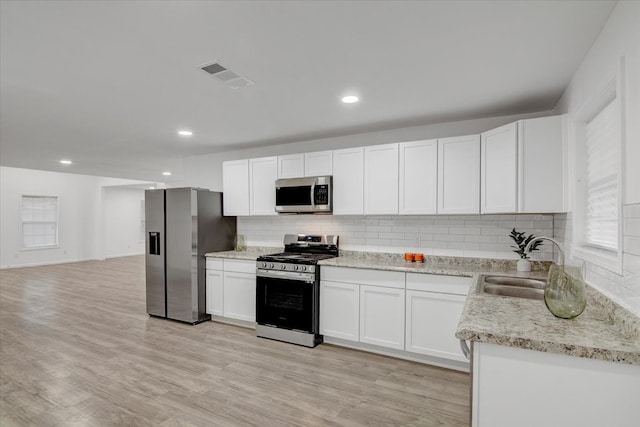 kitchen featuring tasteful backsplash, white cabinets, light wood-type flooring, and appliances with stainless steel finishes