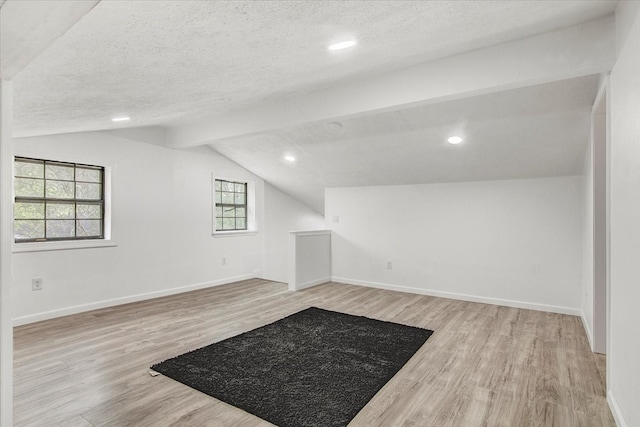 bonus room with lofted ceiling with beams, a healthy amount of sunlight, a textured ceiling, and light wood-type flooring