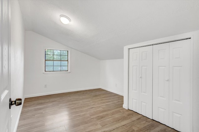 additional living space with a textured ceiling, light hardwood / wood-style floors, and vaulted ceiling