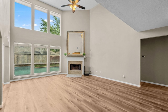 unfurnished living room featuring a fireplace with flush hearth, high vaulted ceiling, baseboards, and wood finished floors