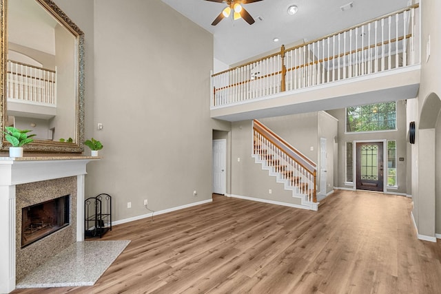 unfurnished living room featuring a high ceiling, baseboards, a fireplace, and wood finished floors