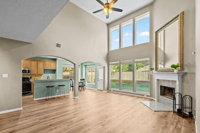 living area featuring visible vents, a ceiling fan, a high end fireplace, light wood-type flooring, and baseboards