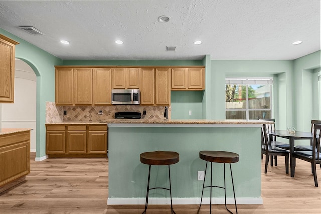 kitchen featuring light wood-style flooring, stainless steel microwave, visible vents, and decorative backsplash