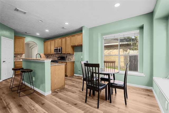 kitchen featuring a kitchen island with sink, visible vents, light wood-type flooring, backsplash, and stainless steel microwave