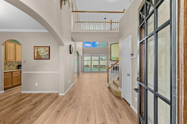 entrance foyer featuring arched walkways, baseboards, light wood-style flooring, stairway, and ornamental molding