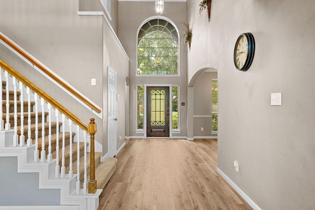 entrance foyer featuring baseboards, arched walkways, a towering ceiling, wood finished floors, and stairs