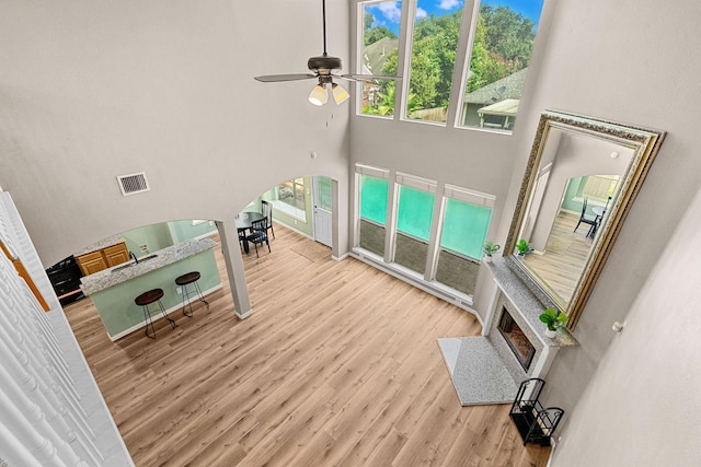 living room with arched walkways, ceiling fan, a high ceiling, wood finished floors, and visible vents