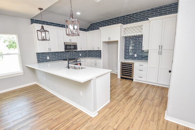 kitchen with pendant lighting, white cabinets, wine cooler, sink, and kitchen peninsula