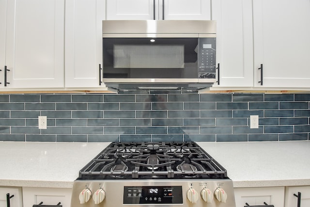 kitchen featuring backsplash, light stone counters, white cabinetry, and stove